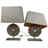 A PAIR OF DESIGNER IRON CIRCULAR WHEEL LAMPS, mounted on bases. One shade needs reattaching. Bulbs