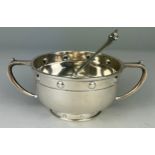 AN UNUSUAL ARTS AND CRAFTS SILVER TWO HANDLE BOWL AND SPOON WITH EMBOSSED ROUNDELS DATED 1927, By