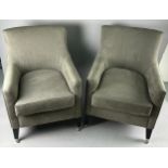 A PAIR OF GREY UPHOLSTERED ARMCHAIRS raised on ebonised legs with castors.