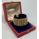 A HIGH CARAT GOLD AND SEED PEARL BANGLE, The reticulated sides studded with over one hundred small