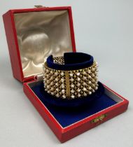 A HIGH CARAT GOLD AND SEED PEARL BANGLE, The reticulated sides studded with over one hundred small