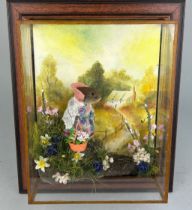 A TAXIDERMY CASED DIORAMA BY TONY ARMISTEAD OF A MOUSE CARRYING A BASKET OF FLOWERS AND WALKING ON A