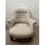 An upholstered tub arm chair with button back on mahogany legs and ceramic castors