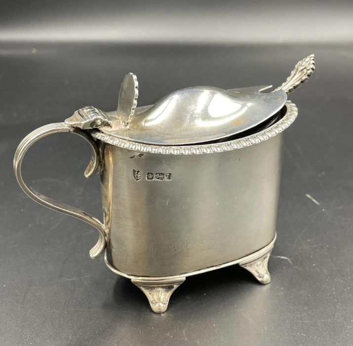 A silver mustard pot with blue glass liner and spoon. Hallmarked for Sheffield 1903 by J & J