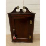 An oak corner hanging cupboard with moulded cornice over a panel door and brass hinges