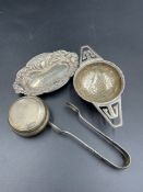 A selection of four silver items to include: pin dish, sugar nips, tea strainer and small lidded