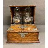 An oak two decanter tantalus with double hinged lids to front to reveal a partitioned storage