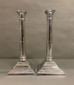 A pair of white metal column candle sticks on square bases