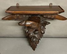 A black forest carved eagle with wide spread wings and clock shelf above sitting below acorns and