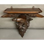 A black forest carved eagle with wide spread wings and clock shelf above sitting below acorns and