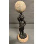 A bronze and marble statue of a boy holding a marble ball above his head