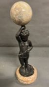 A bronze and marble statue of a boy holding a marble ball above his head