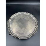 A hallmarked silver tray with scalloped edge on three ball and claw feet with engraved design,