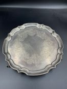 A hallmarked silver tray with scalloped edge on three ball and claw feet with engraved design,