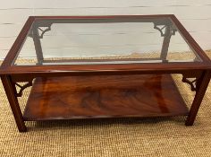 A glass coffee table with carved corner supports and shelf under (H49cm W114cm D73cm)