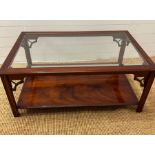 A glass coffee table with carved corner supports and shelf under (H49cm W114cm D73cm)
