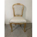 A baroque style gold painted dining room chair upholstered in white