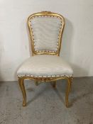 A baroque style gold painted dining room chair upholstered in white