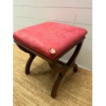 A Victorian mahogany stool on cross over supports, upholstered in red fabric