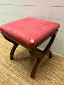 A Victorian mahogany stool on cross over supports, upholstered in red fabric