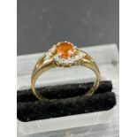 An orange sapphire and cubic zirconia cluster ring, central oval cut orange sapphire weighing on