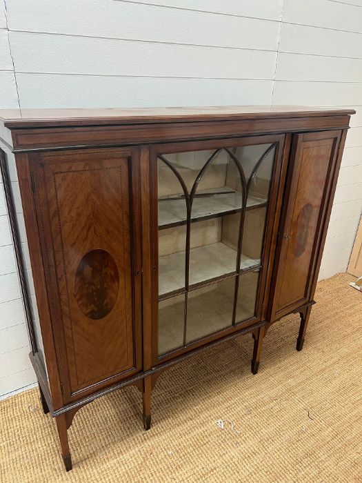 A display cabinet with gazed door to centre flank by two panelled doors on tapering legs with