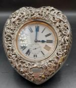 An 1899 heart shaped silver pocket watch stand on easel back with overlarge pocket watch.