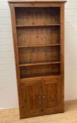 A three shelf stained pine book case with two door cupboard under (H200cm W90cm D32cm)
