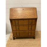 An oak three drawer bureau with brass drop handles on bun feet (H100cm W74cm D24cm)