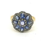 A yellow metal ring with a silver set head of sapphires and diamonds shaped like a flower head. Size