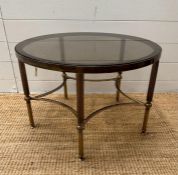 A circular Mid Century smoked glass coffee/stick table on reeded brass support on pentagram