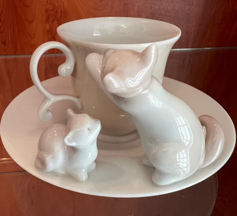 A Lladro cup and saucer with cats playing to side