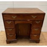 An oak kneehole desk with centre cupboard flanked by three drawers to left and right with brass drop