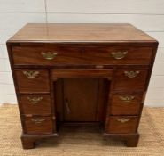 An oak kneehole desk with centre cupboard flanked by three drawers to left and right with brass drop
