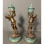 A pair of French bronze cherubs holding ceramic hand painted foliate vases on plinth H29.5cm