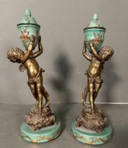 A pair of French bronze cherubs holding ceramic hand painted foliate vases on plinth H29.5cm