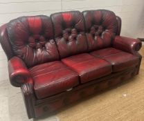 A burnt red leather button back three seater sofa and matching reclining arm chair