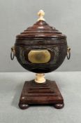 A carved lidded urn on stepped base with four bun feet and two handles, ivory finial and support (