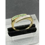 An emerald and cubic zirconia yellow metal half eternity ring. Grain set with a row of eight round
