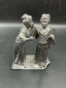 A white metal statue of two Geisha girls