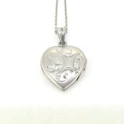 An engraved heart shaped opening locket suspended by a bale on a platinum chain. The heart is marked