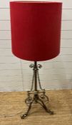 A brass floor standing lamp with scrolling details and red shade