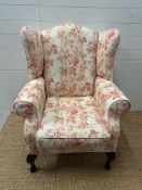 A white ground floral upholstered wing back arm chair on cabriole legs (H110cm W78cm D70cm)