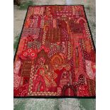 An Indian needlework panelled textile in reds and pinks silks and cottons with mirrored inlay and