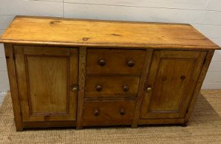 A Victorian pine dresser base with three drawers flanked by cupboards (H75cm W145cm D50cm)