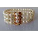 A cultured pearl triple strand bracelet, 18 cm, with a gold and ruby clasp, 23 x 15mm, stamped 750,