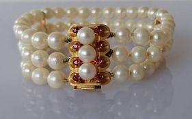 A cultured pearl triple strand bracelet, 18 cm, with a gold and ruby clasp, 23 x 15mm, stamped 750,