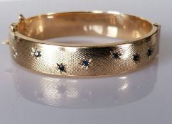 A star-set sapphire and gold bangle with engine turned decoration, 60mm, hallmarked 9ct, 24.3g