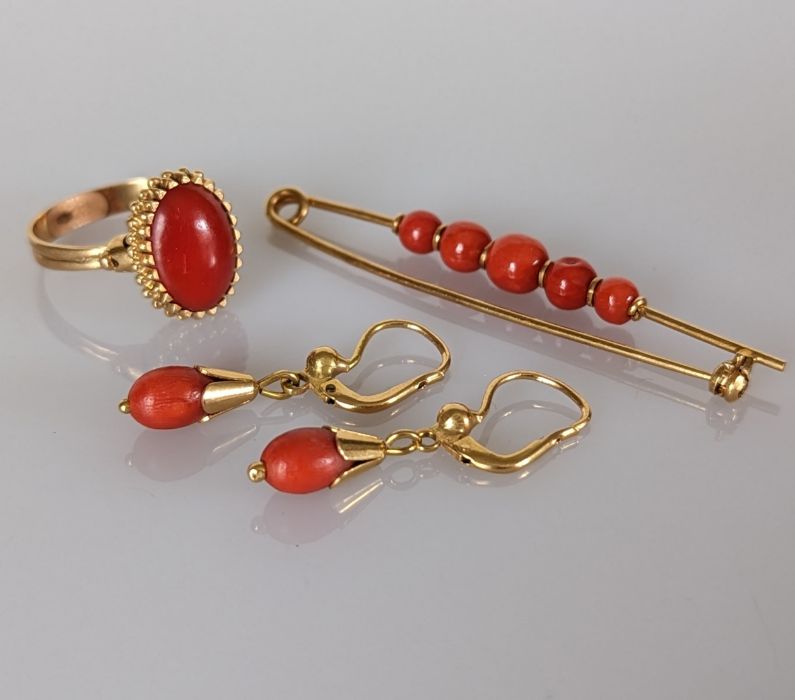 A yellow gold and coral cabochon oval ring in a basket setting with similar brooch and earrings