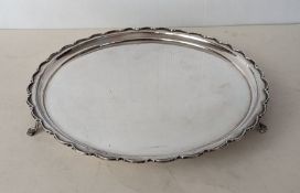 A George V circular silver salver with applied carved decoration to rim, on three lion paw feet